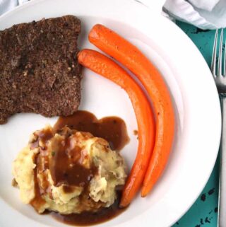 overhead view of cube steak recipes with cube steak, two carrots, and mashed potatoes on a white plate