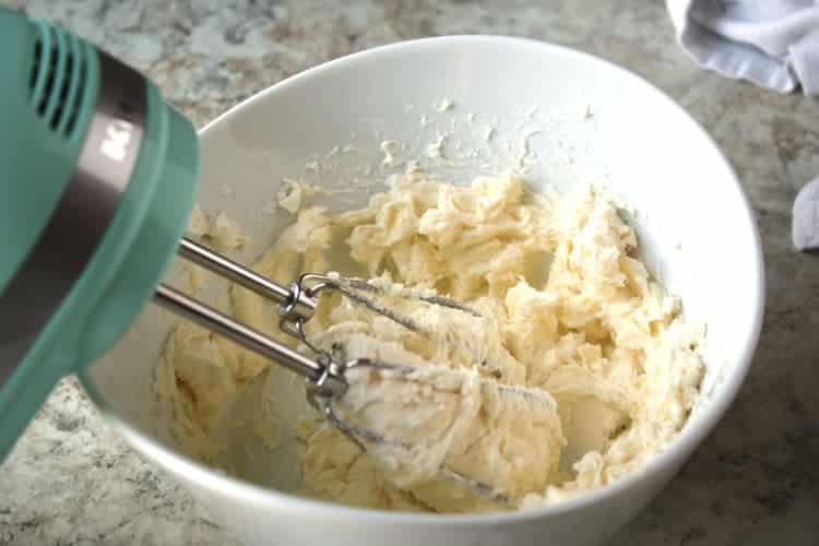 closeup of easy cream cheese frosting in a white bowl being beaten by a green mixer