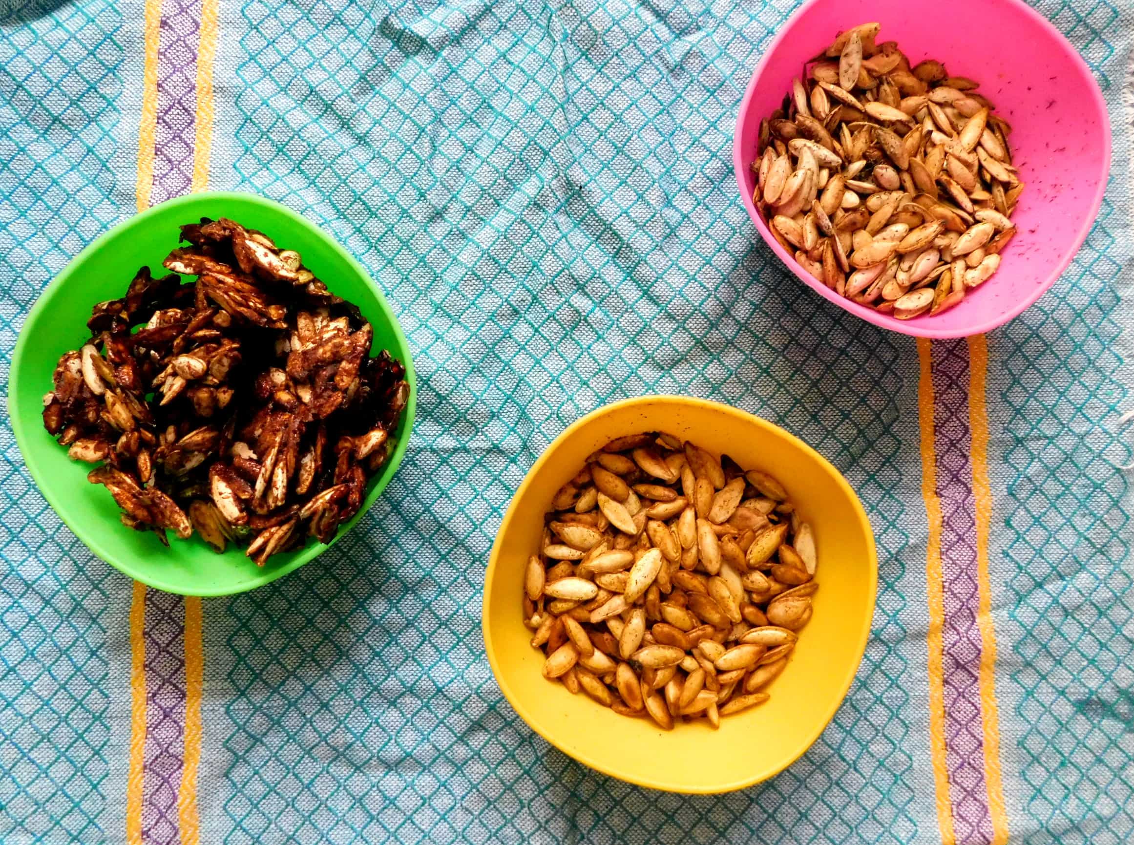 Three bowls of roasted pumpkin seeds in maple pumpkin spice, Indian spiced, and dill and vinegar flavors