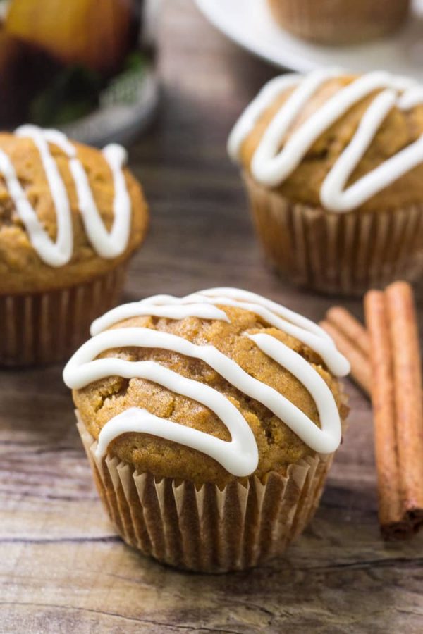 Pumpkin muffins drizzled with cream cheese glaze on a wooden table with cinnamon sticks