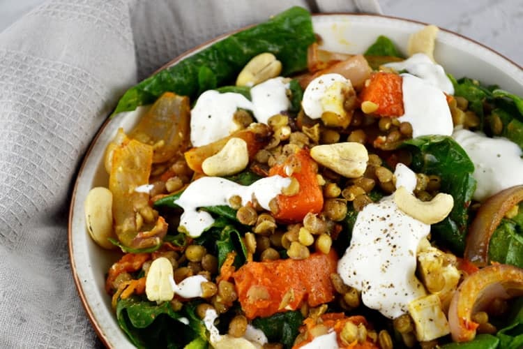 A close up shot of a squash salad with feta cheese, lentils and spinach and a sour cream dressing