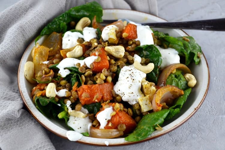 Close up of a squash salad with feta cheese, lentils and spinach grey towel in background