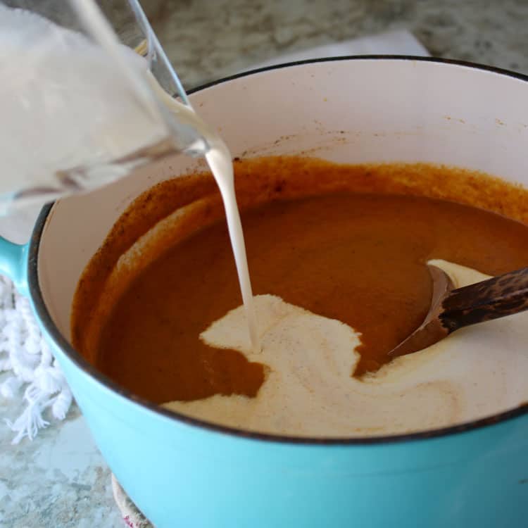 heavy cream pouring out of measuring cup into a blue pot of carrot soup