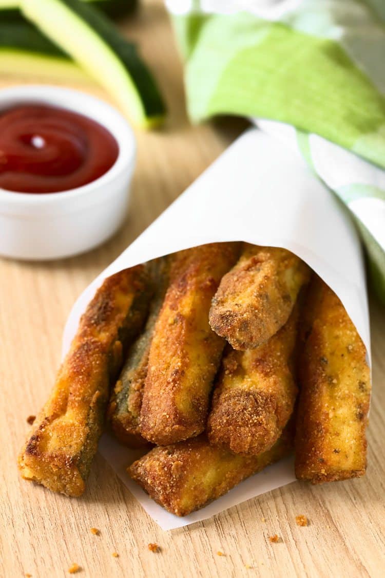 fried zucchini sticks wrapped in parchment paper with ketchup on the side