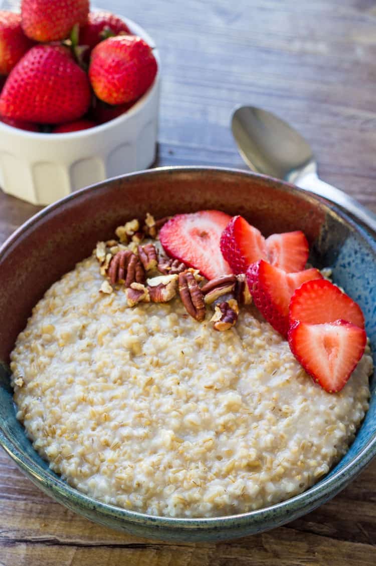 Instant Pot steel cut oats in a bowl next to a spoon and a bowl of fresh strawberries