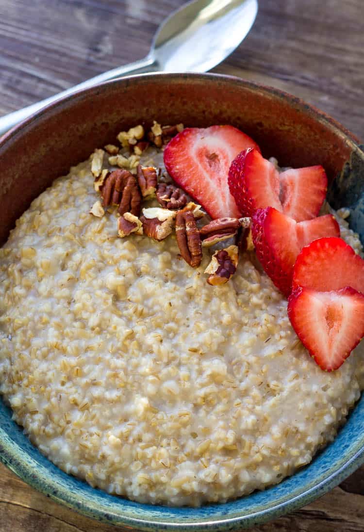 Instant Pot Steel Cut Oats in a bowl topped with strawberries and pecans next to a spoon