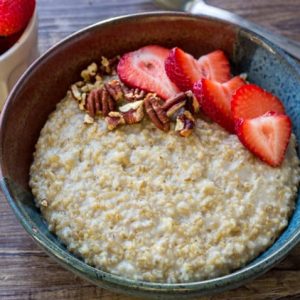 Horizontal shot of Instant Pot steel cut oats in a ceramic bowl with sliced strawberries and pecan pieces