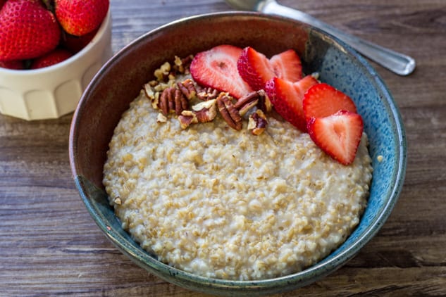 Horizontal shot of Instant Pot steel cut oats in a ceramic bowl with sliced strawberries and pecan pieces