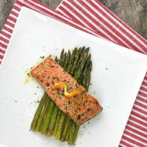 salmon plated over asparagus on white square plate
