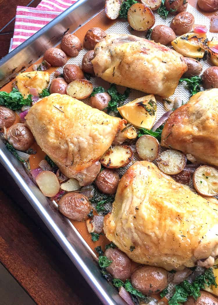 overhead view of sheet pan covered with herb-roasted chicken thighs, halved potatoes, and sprigs of thyme