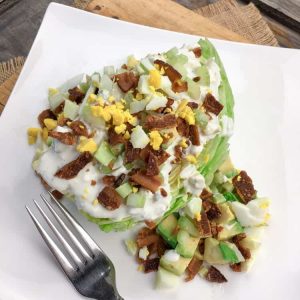 keto salad on a white plate consisting of iceberg lettuce, bacon, and eggs next to a fork
