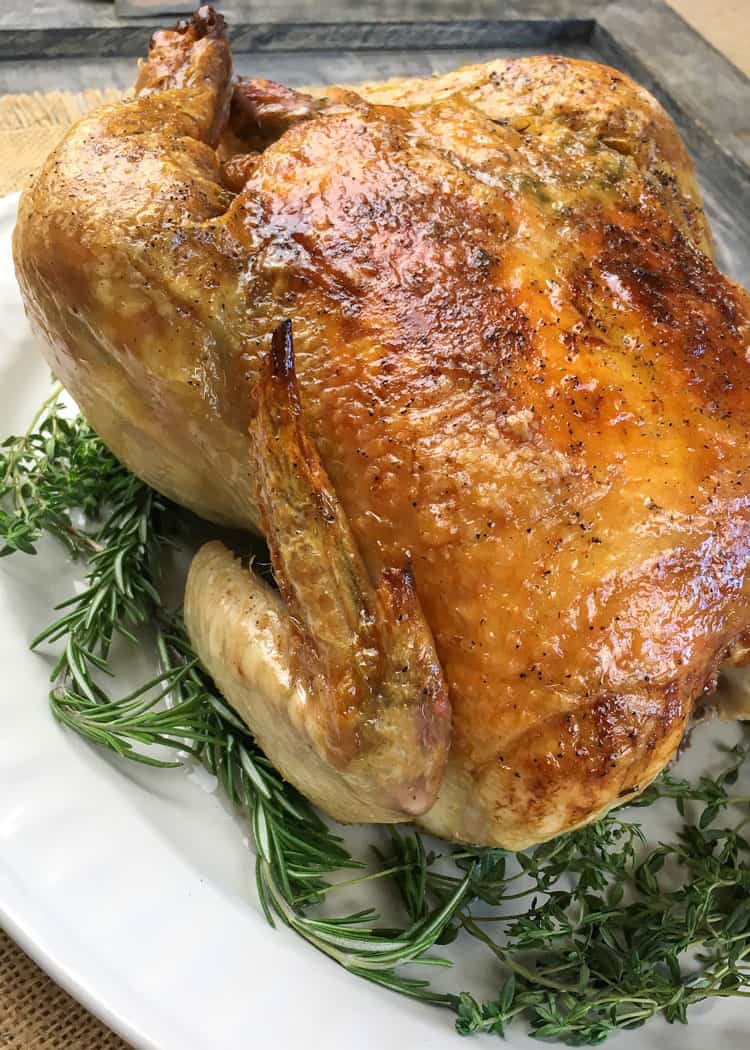 closeup of roasted keto chicken in a bed of herbs on top of a white round plate