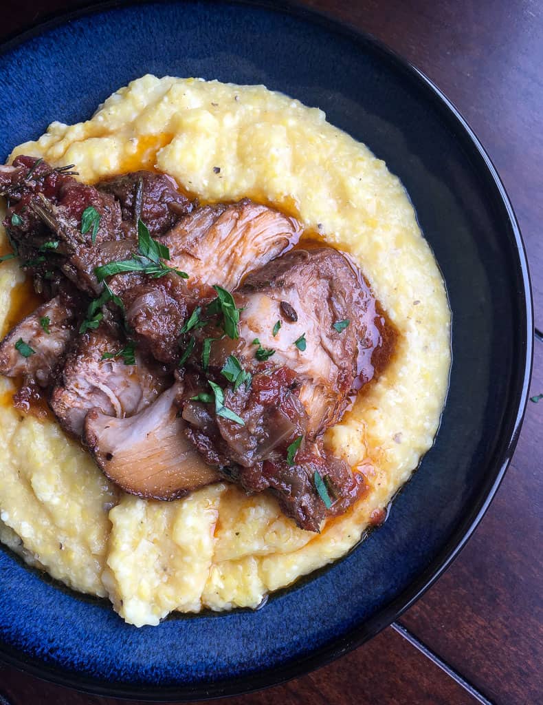 sliced roasted pork butt on creamy polenta on a blue plate