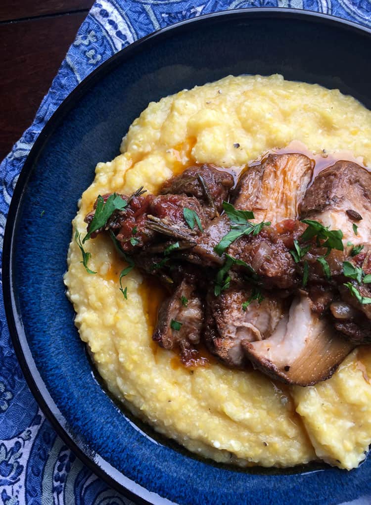 sliced roasted pork butt on creamy polenta on a blue plate