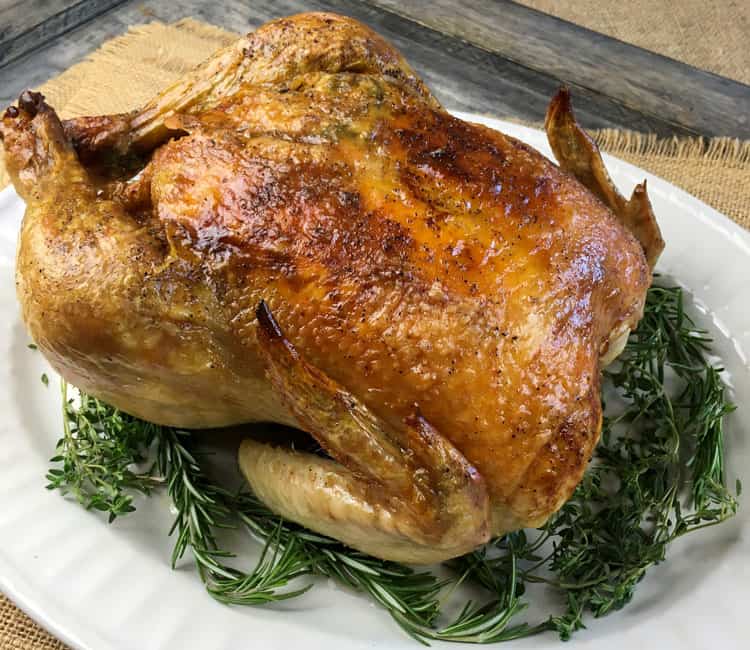 crispy roasted keto chicken surrounded by rosemary and thyme on a round white platter