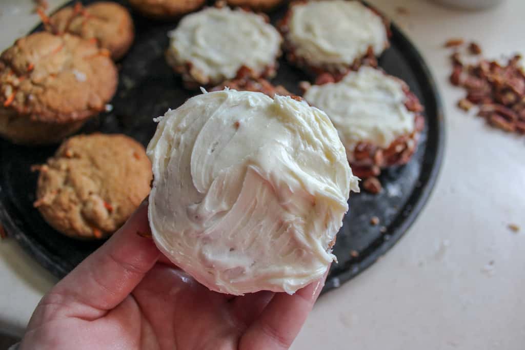 hand holding carrot cake cookies with white frosting on top