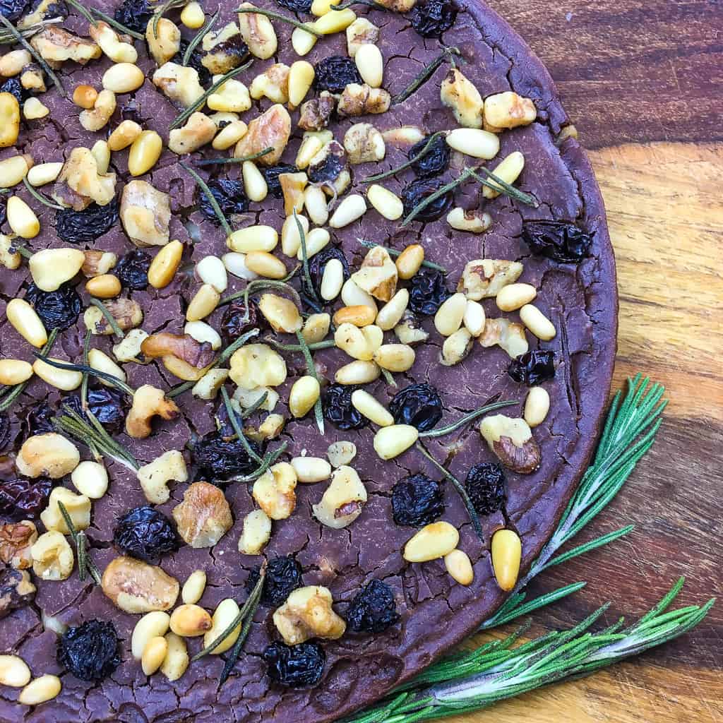 closeup of whole Castagnaccio cake next to sprigs of rosemary on a cutting board