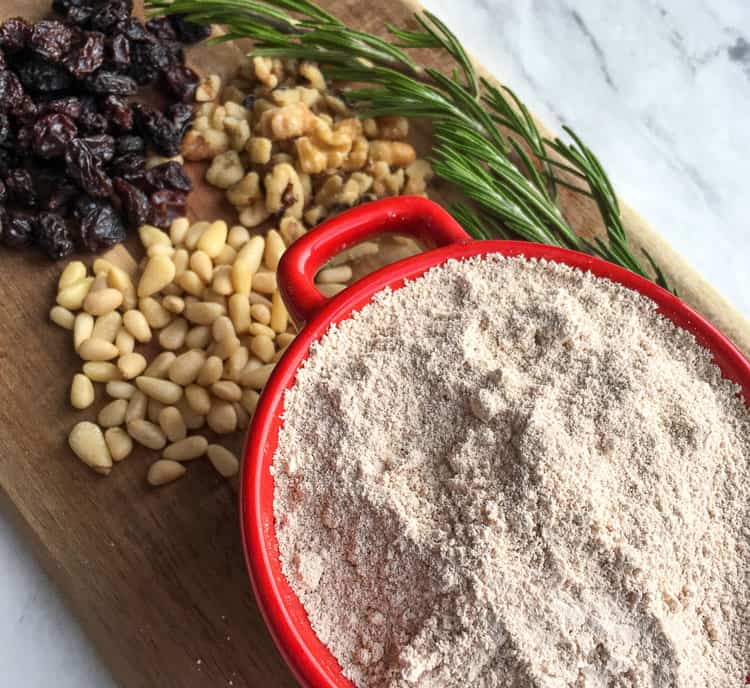 closeup of chestnut flour in a red bowl next to other ingredients on a cutting board for Castagnaccio