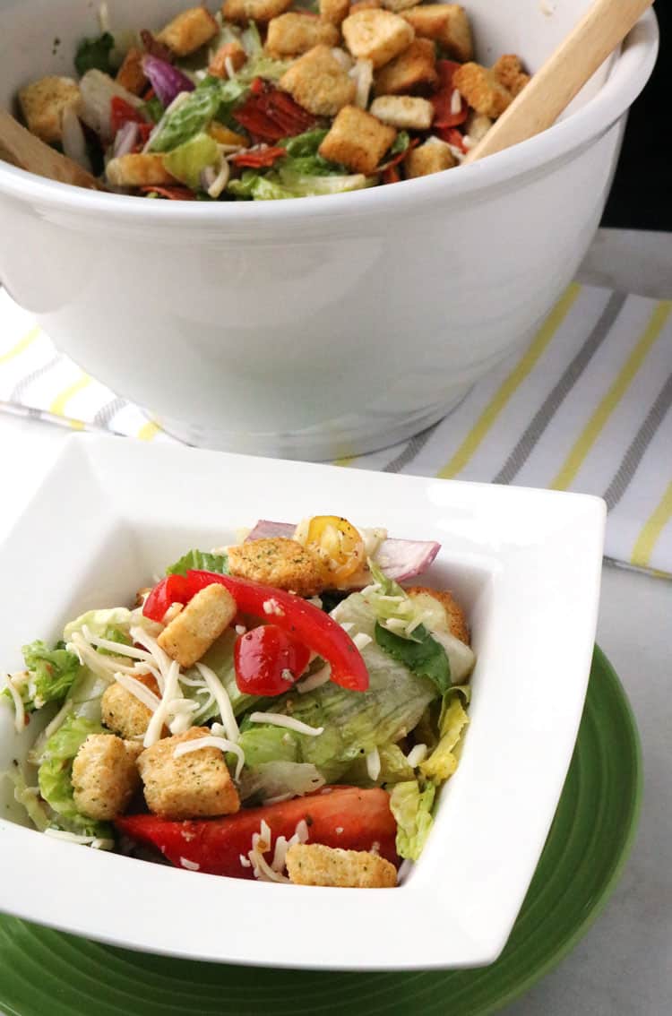 Italian salad in white mixing bowl, with a portion served in white salad bowl on top of a green plate.