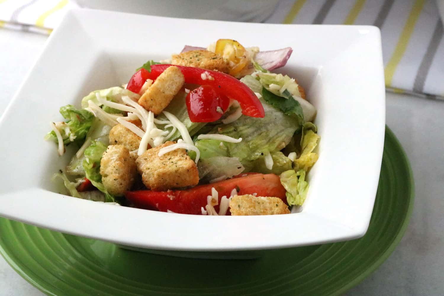 Italian Salad with Homemade Dressing served in a white bowl on top of a green plate.