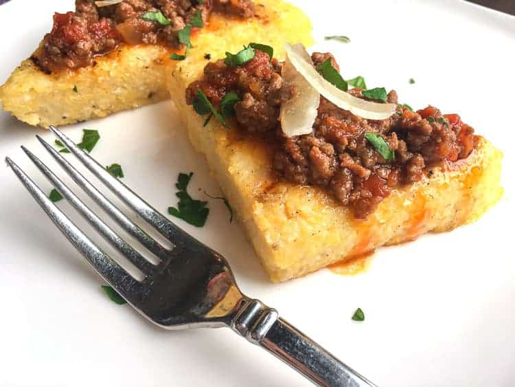 closeup of polenta crostini with meat on top next to a fork