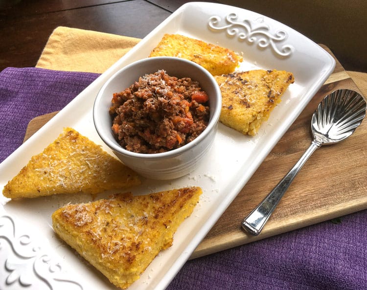 white platter containing polenta slices and a small bowl of sausage ragu in the middle