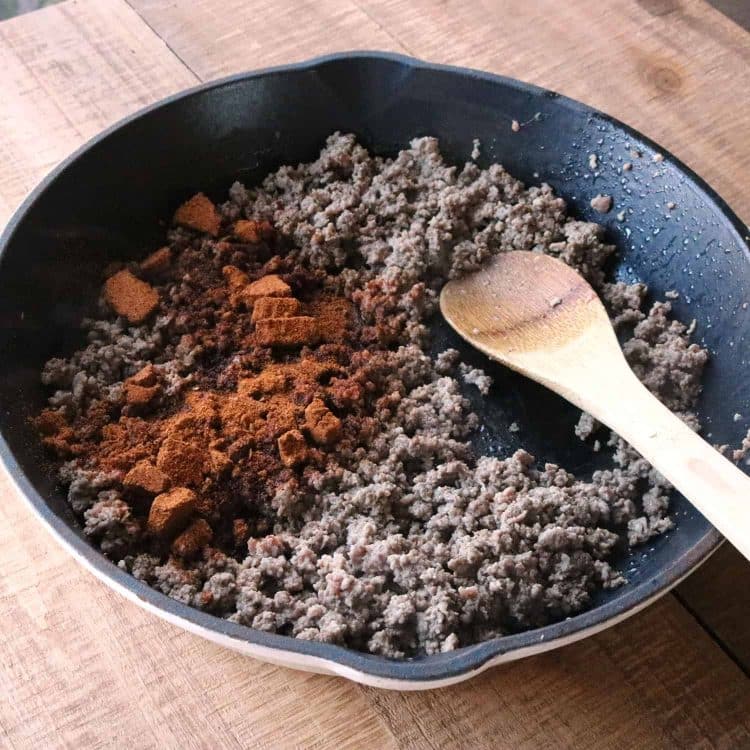 wooden spoon in an iron skillet with cooked ground beef covered in taco seasoning for mexican pizza