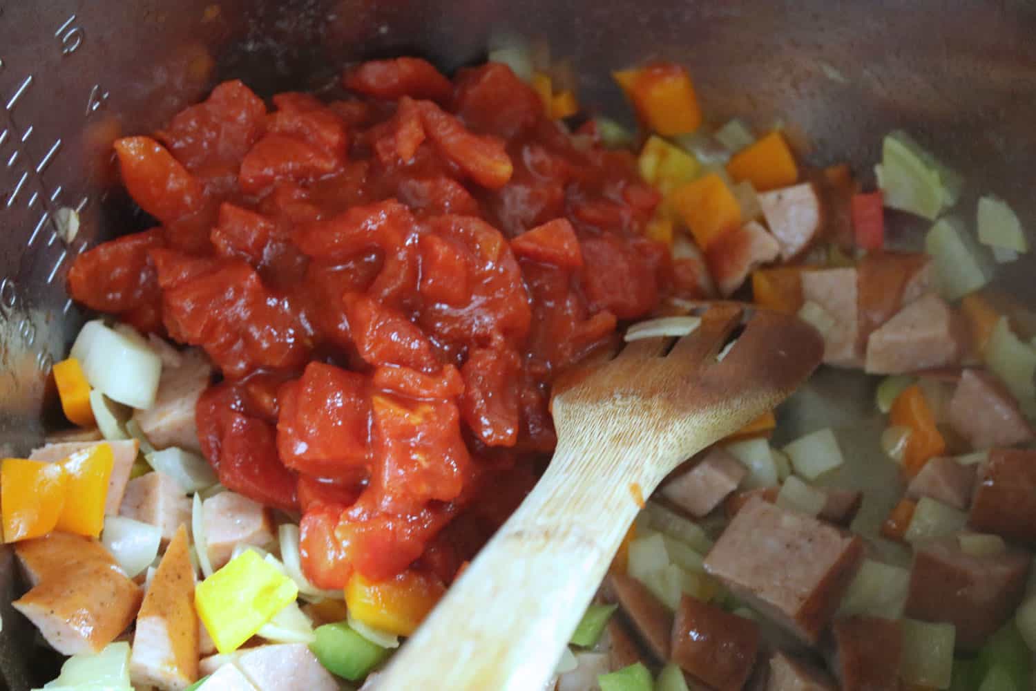 chopped bell peppers, onions, sausage and diced tomatoes being stirred by a wooden spoon