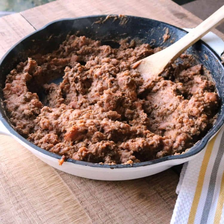 cooked ground beef and refried beans mixed in an iron skillet with a wooden spoon for mexican pizza filling