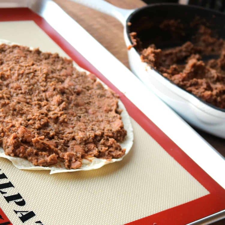 bottom tortilla of a mexican pizza covered with refried beans and ground beef mixture on a silicon cooking sheet