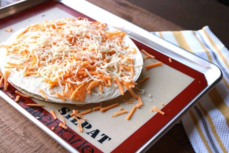 uncooked mexican pizza topped with shredded white and yellow cheese on a silicon baking sheet