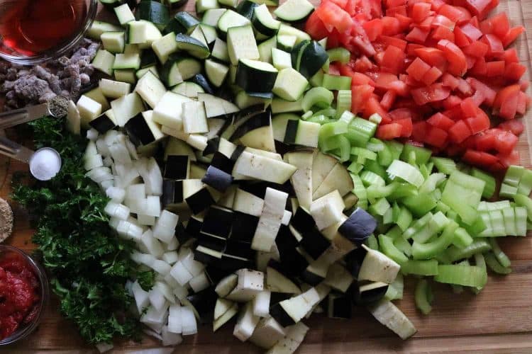 Overhead view of chopped eggplant, celery, tomatoes, herbs, vinegar, tomato paste, onion, salt and pepper