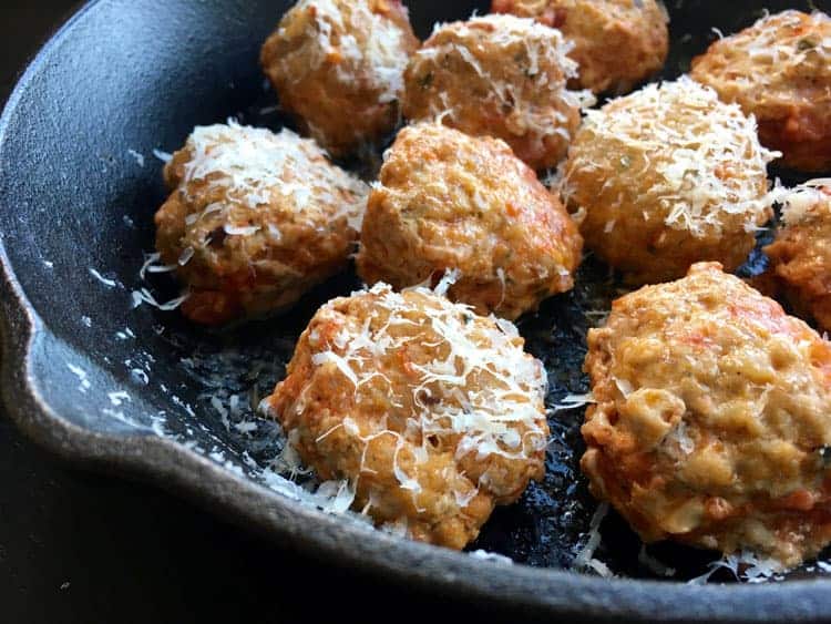 pan containing baked meatballs without breadcrumbs with melted parmesan cheese on top