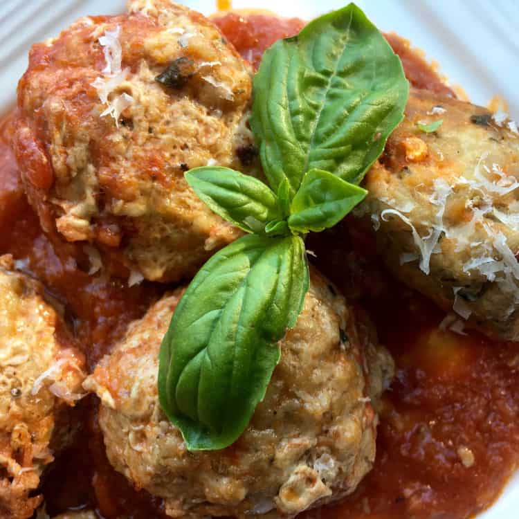 closeup of cooked meatballs without breadcrumbs with a sprig of basil on top
