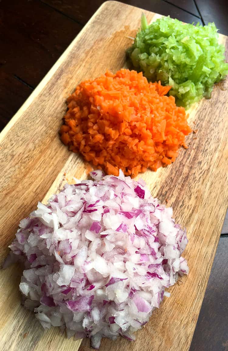minced red onions, carrots, and celery on a cutting board for usage in sausage ragu