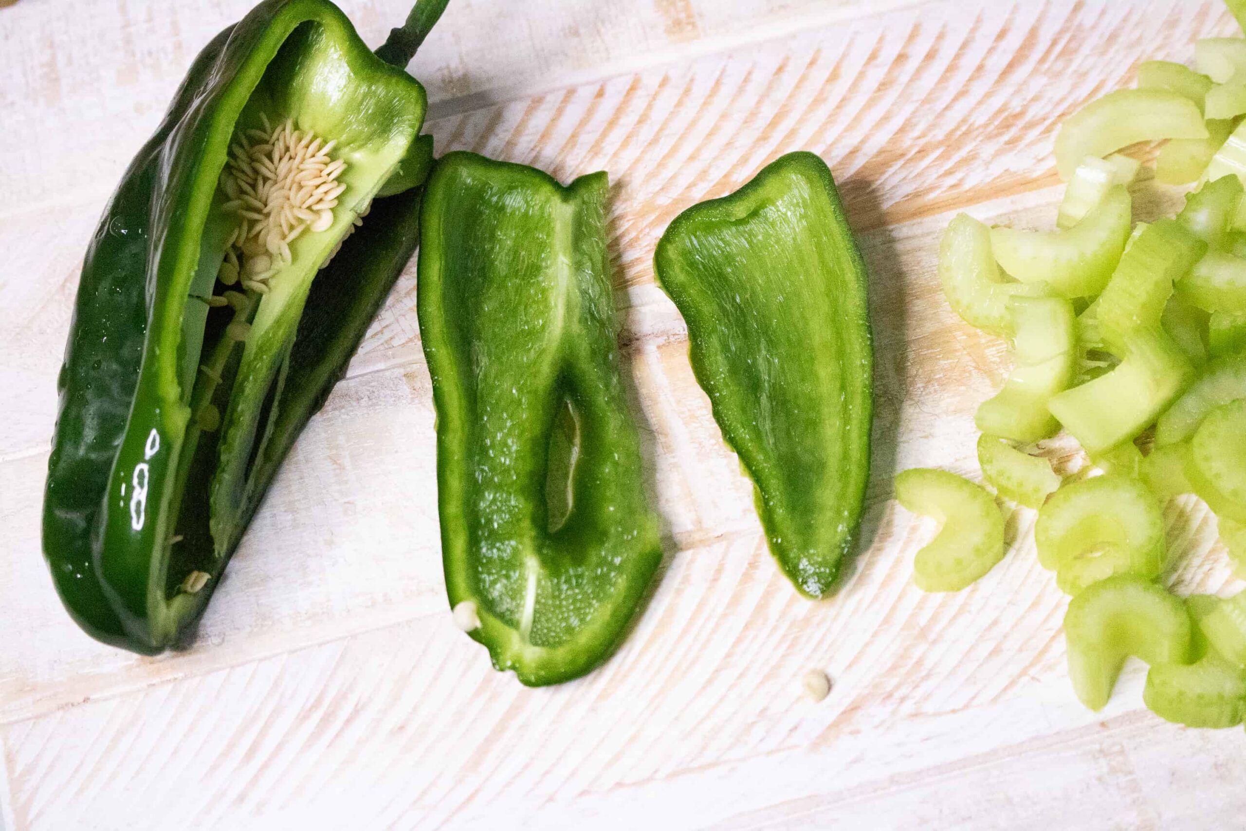Halved Poblano pepper and sliced celery on a white cutting board