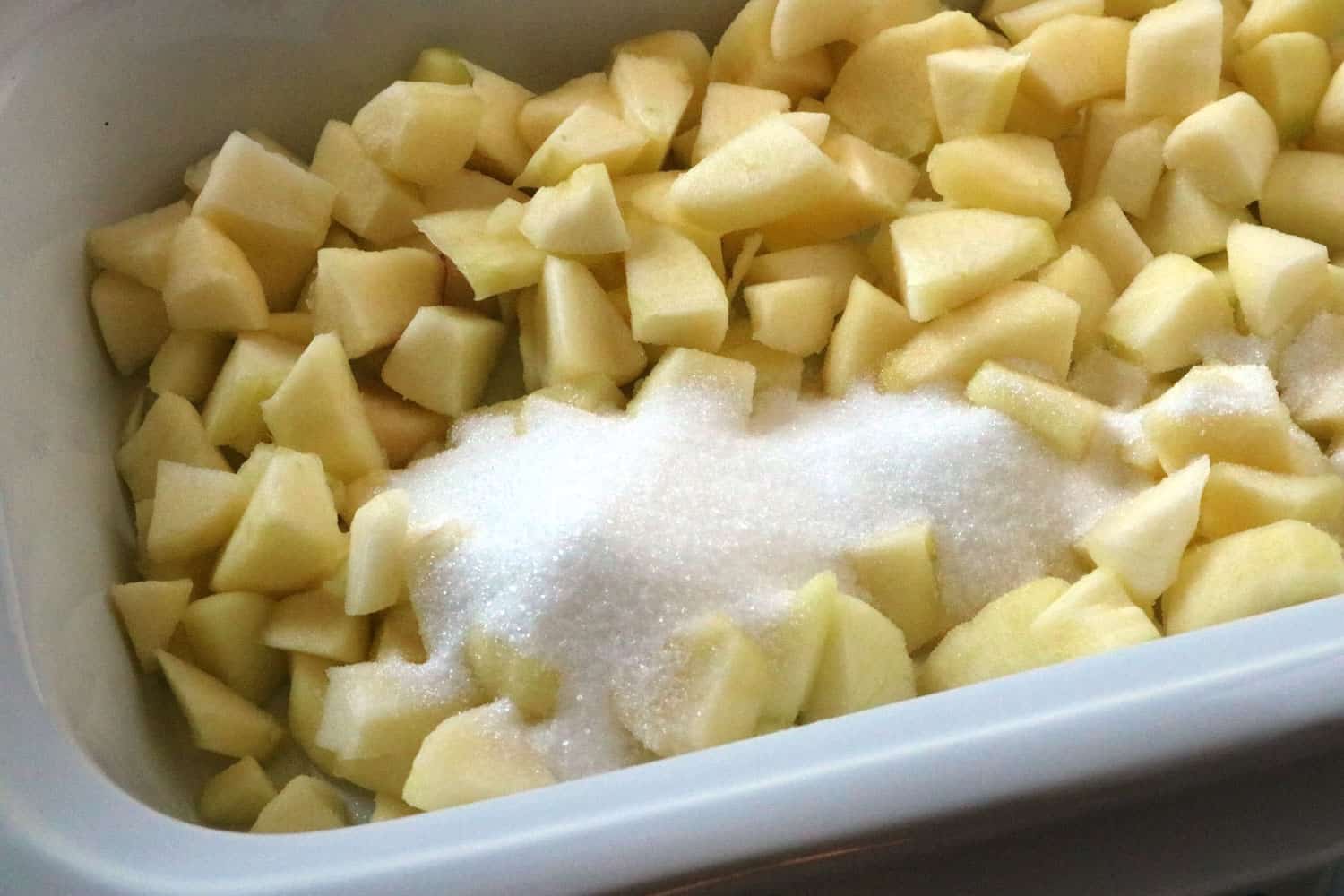 Diced apples and sugar in slow cooker for bread pudding recipe.
