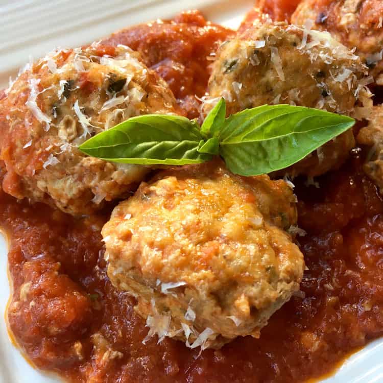 cooked meatballs without breadcrumbs in thick tomato sauce with a sprig of basil on top