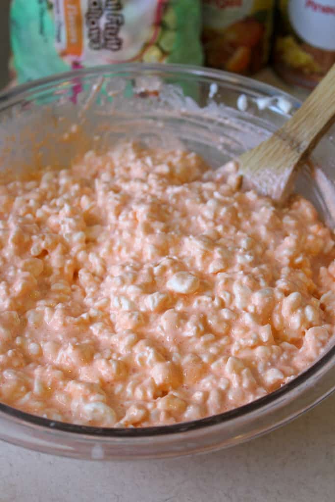 orange fluff salad in a clear bowl with a mixing spoon