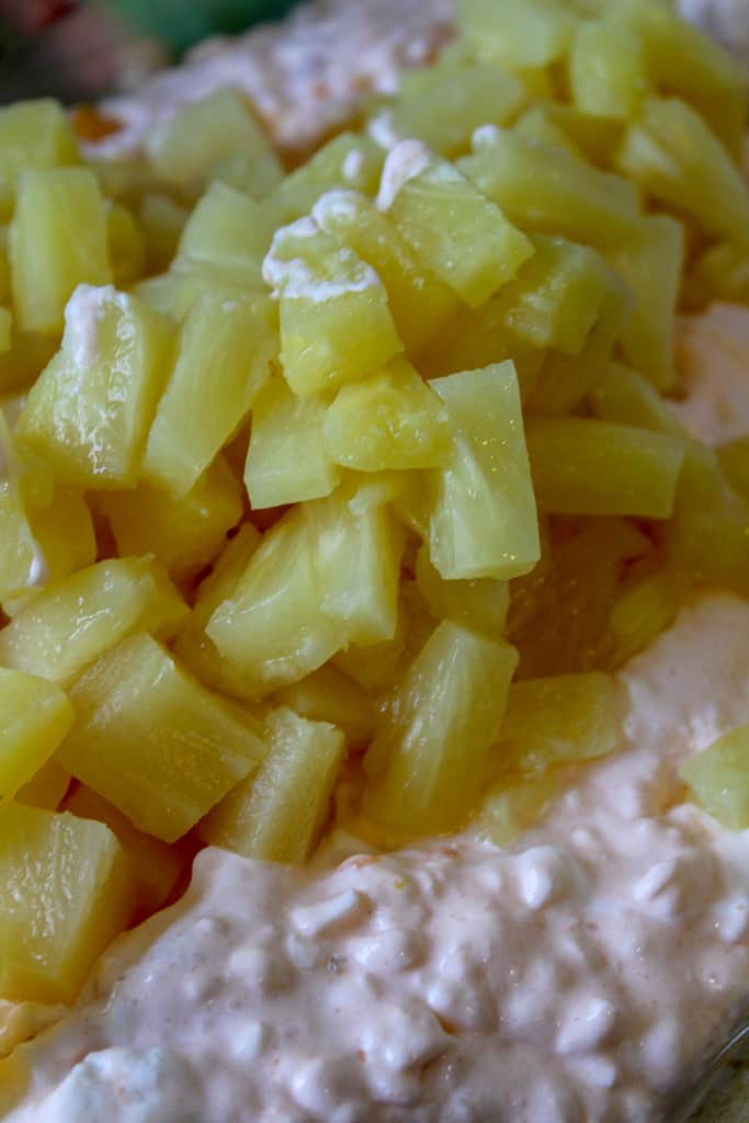 mixing in pineapple tidbits into orange fluff salad