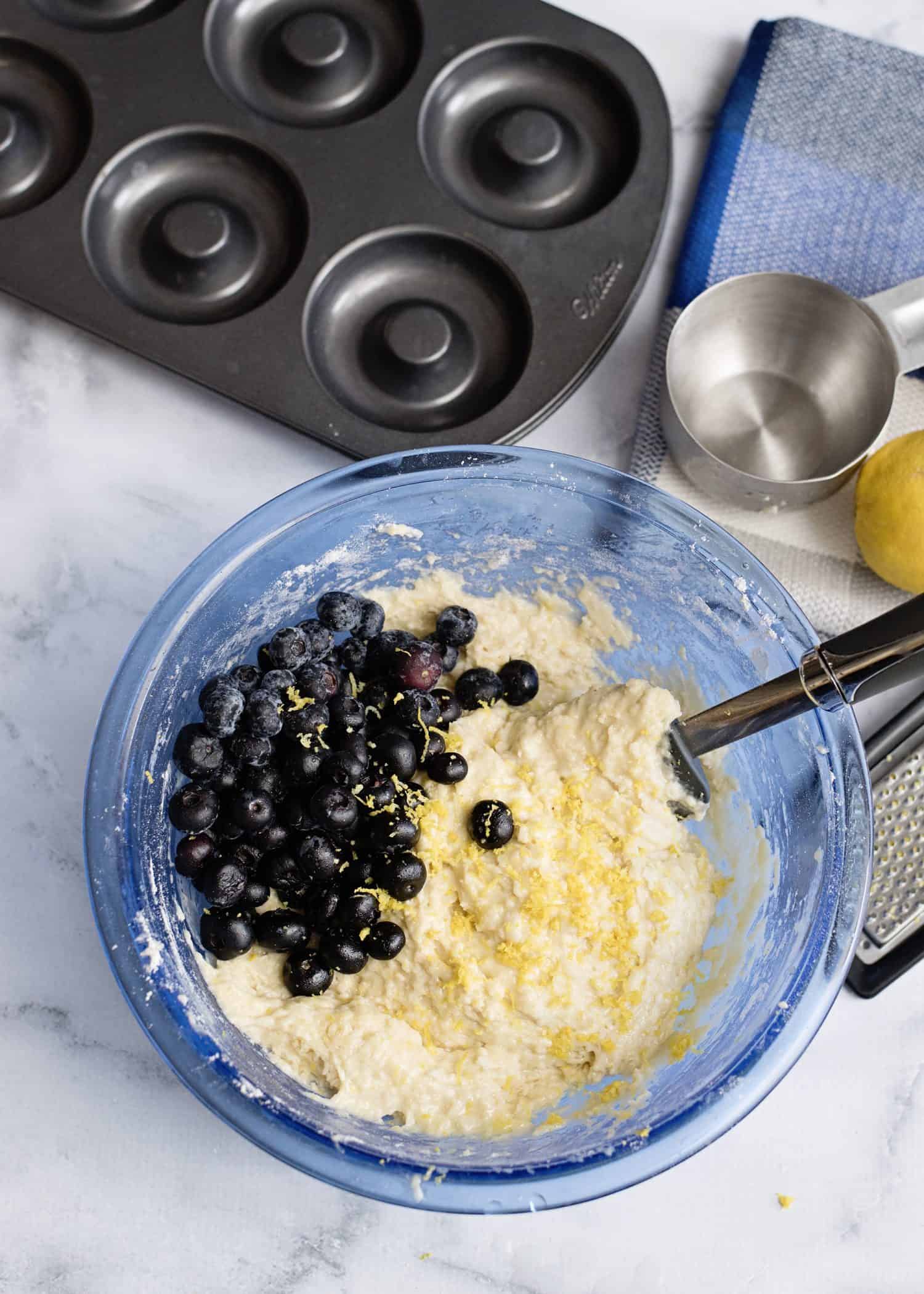 donut baking pan, blue mixing bowl with blueberries being mixed into batter