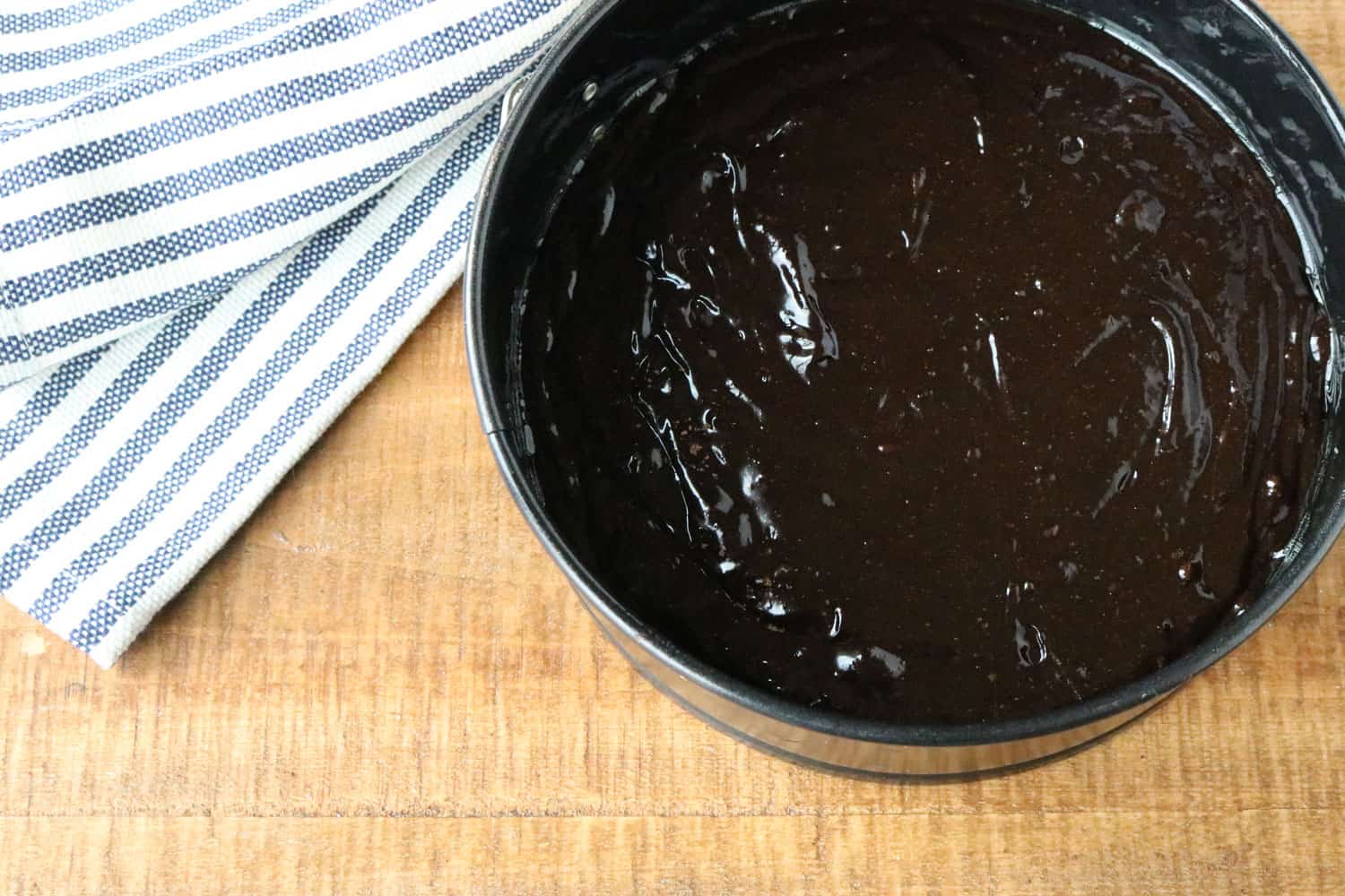 chocolate gluten free cake mixture in a pan on the counter next to a blue and white stripped kitchen towel