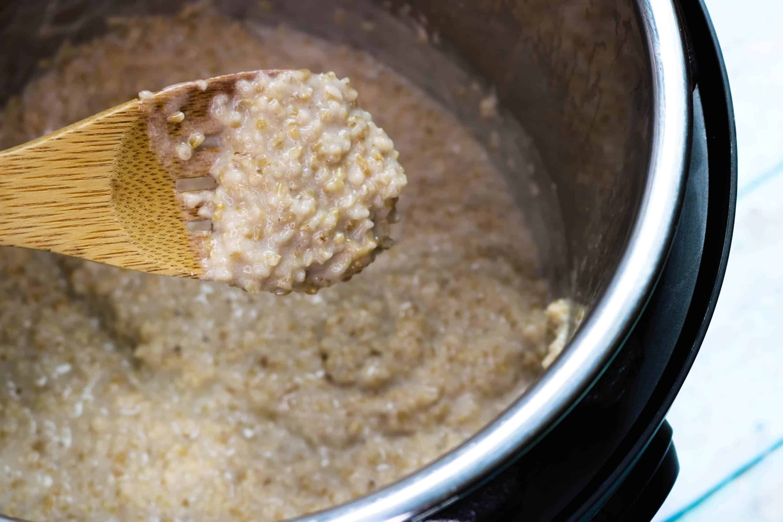 cooked steel cut oatmeal in the Instant Pot inner pot with a scoop on a wooden spoon