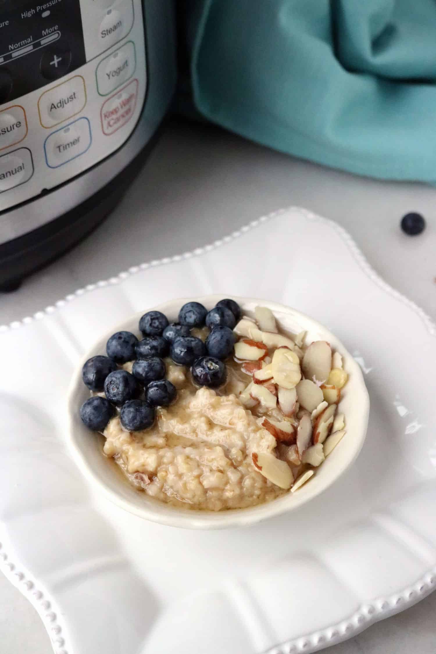Instant Pot steel cut oats topped with blueberries, almonds and honey served in a white bowl on a square white plate