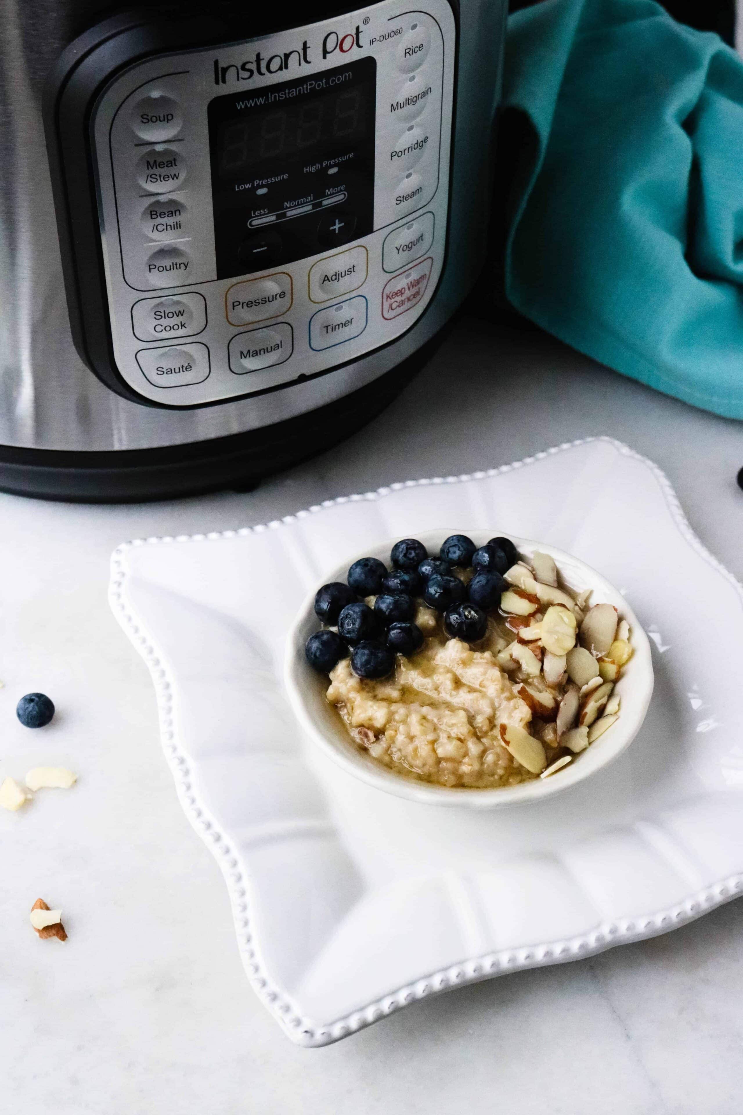 Oatmeal topped with blueberries, almonds and honey served in a white bowl on a square white plate