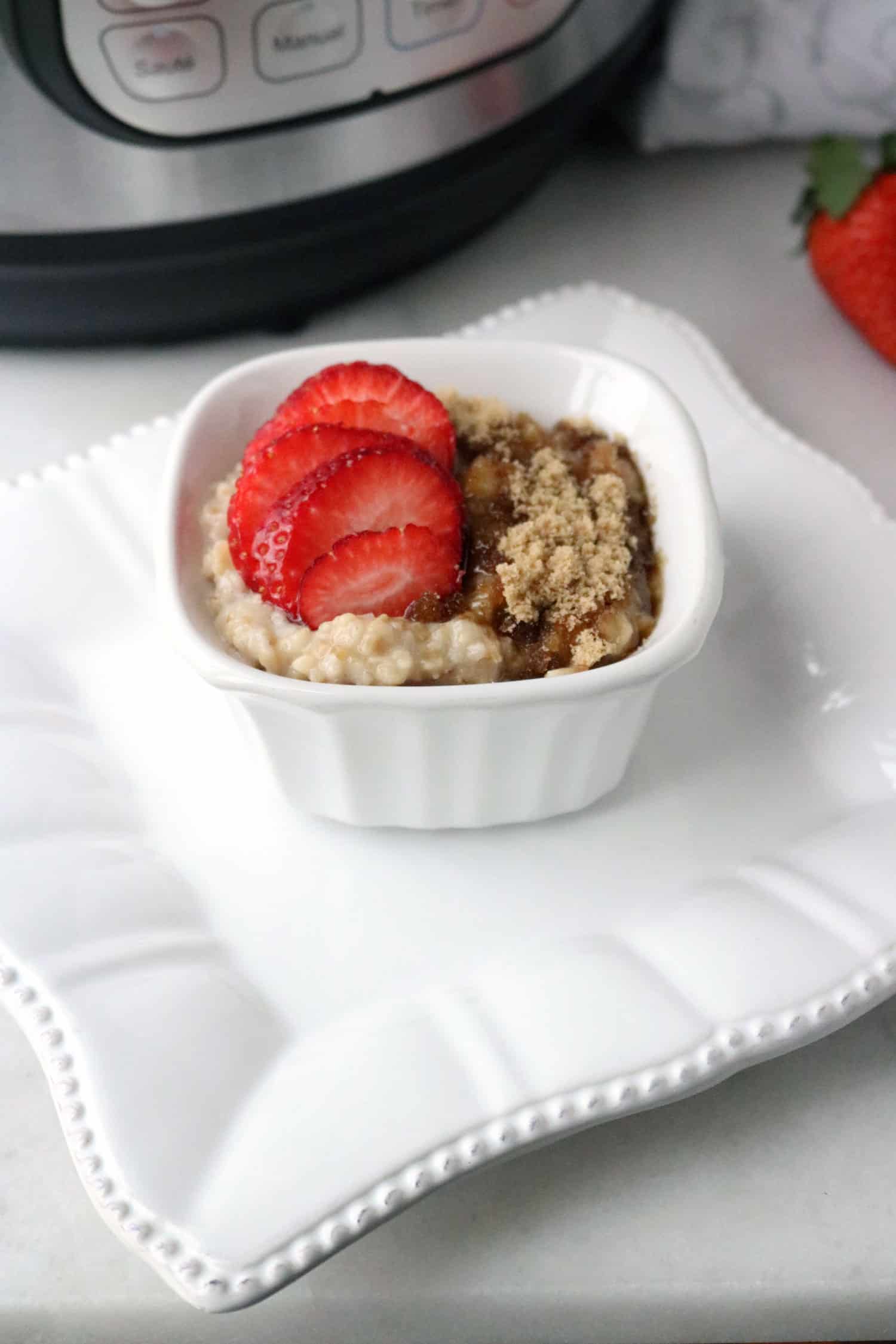 Instant Pot steel cut oatmeal topped with sliced strawberries and brown sugar and served in a white bowl placed on a square white plate