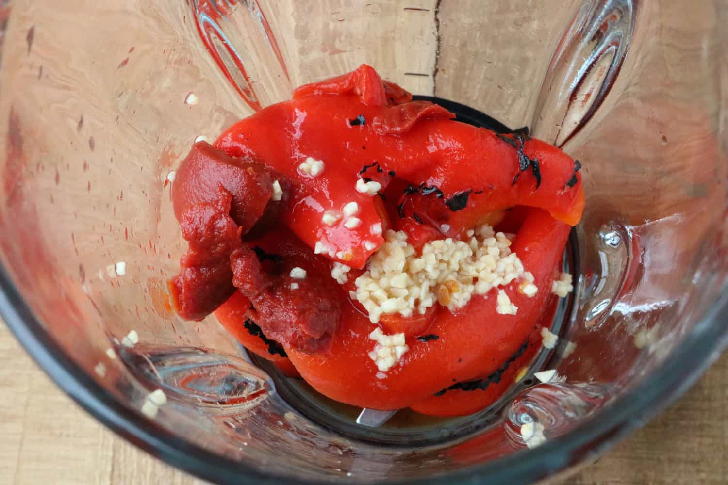 food processor pitcher with roasted red pepper, tomato sauce and garlic in preparation of blending to make roasted red pepper dip