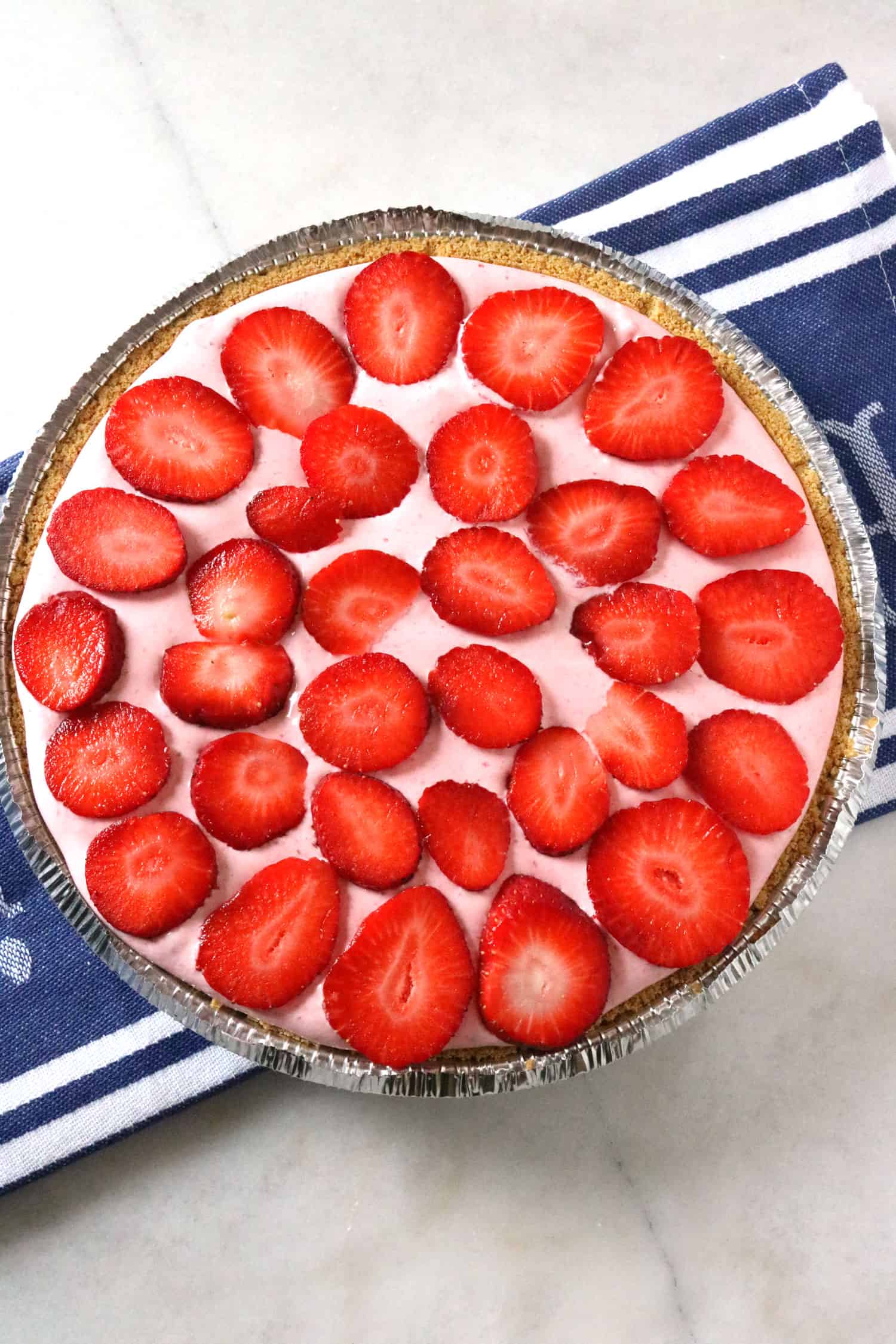 finished pie topped with fresh strawberry slices sitting on blue and white striped towel
