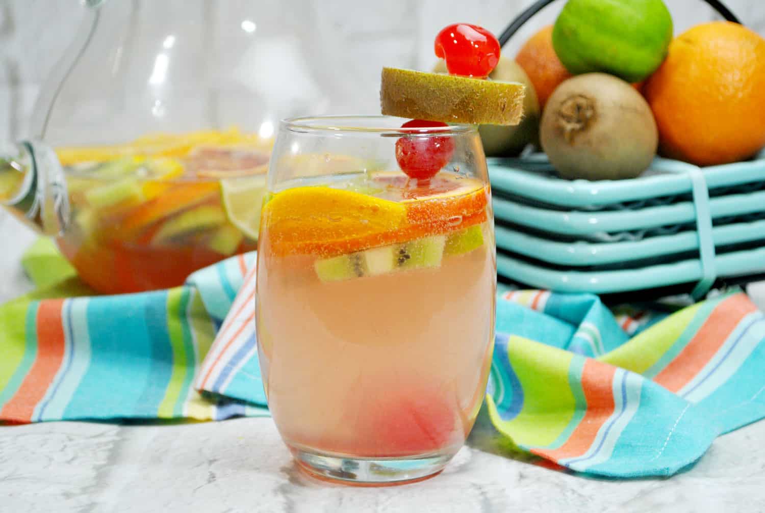 clear glass with peach colored tropical fruity sangria recipe garnished with cherries and oranges