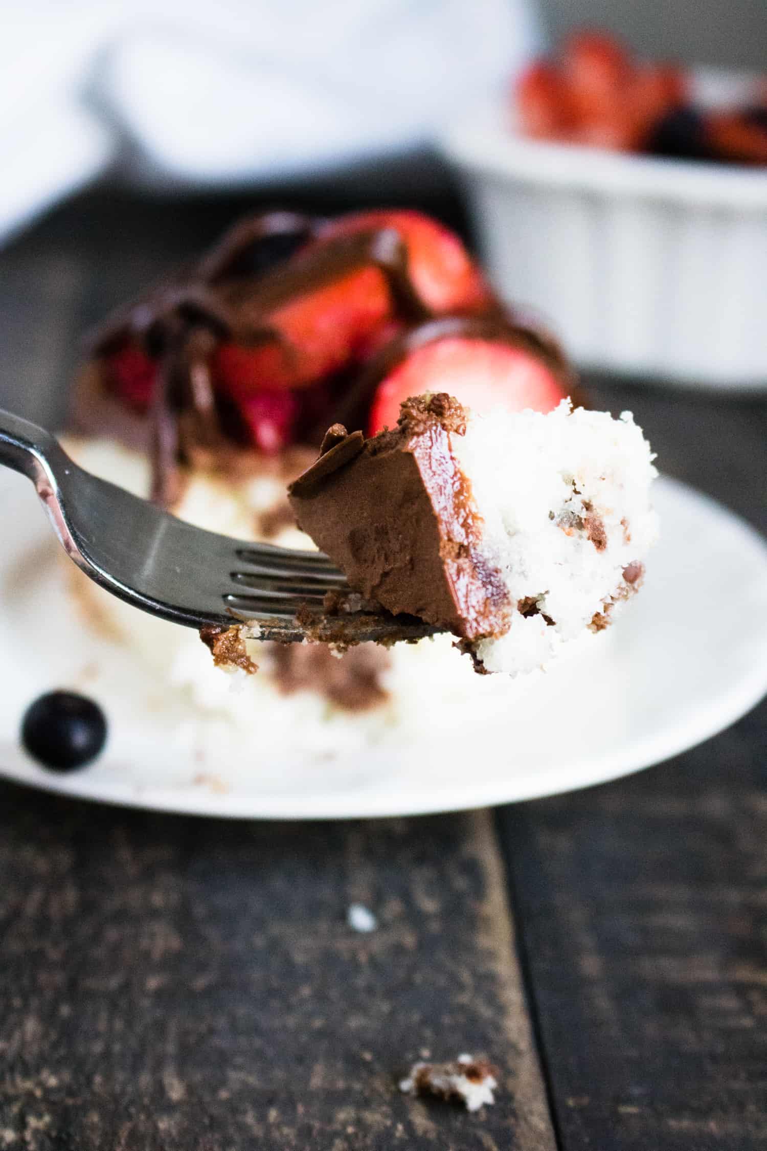 Forkful of chocolate ganache poke cake with berries held over a white plate